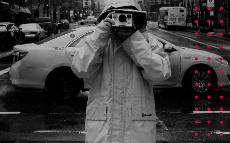 Man holding camera to face viewer in black and white